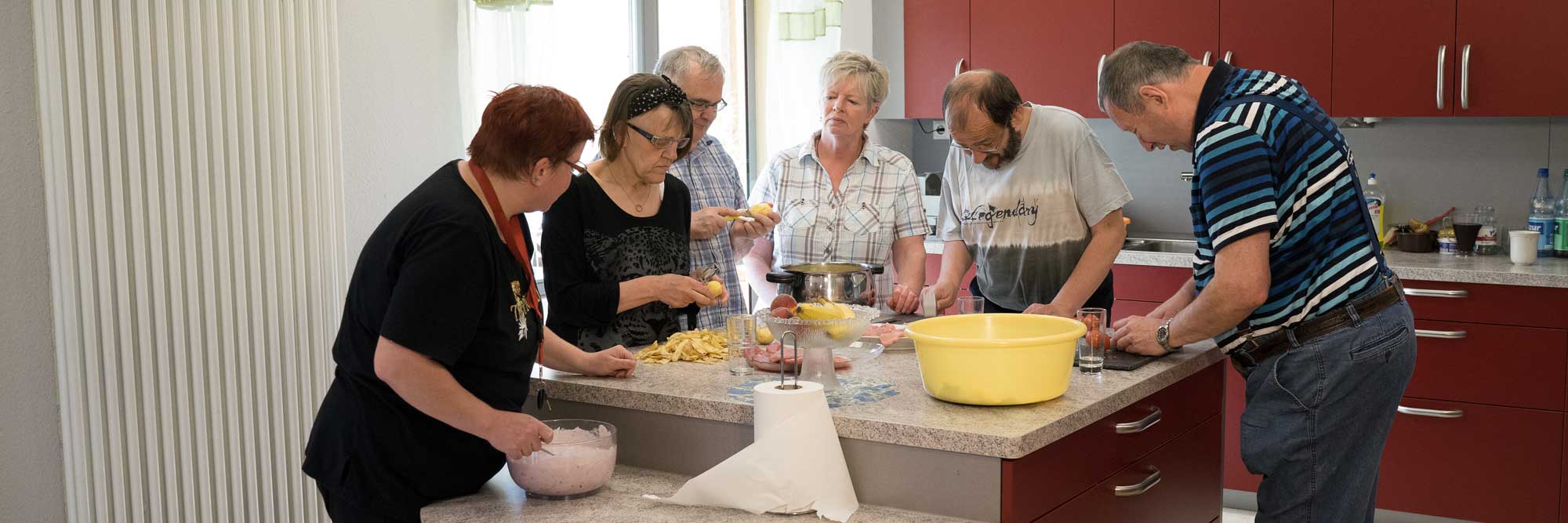 Eine Gruppe von Menschen sitzt auf der Terrasse an einem Tisch und nimmt gemeinsam eine Mahlzeit ein.