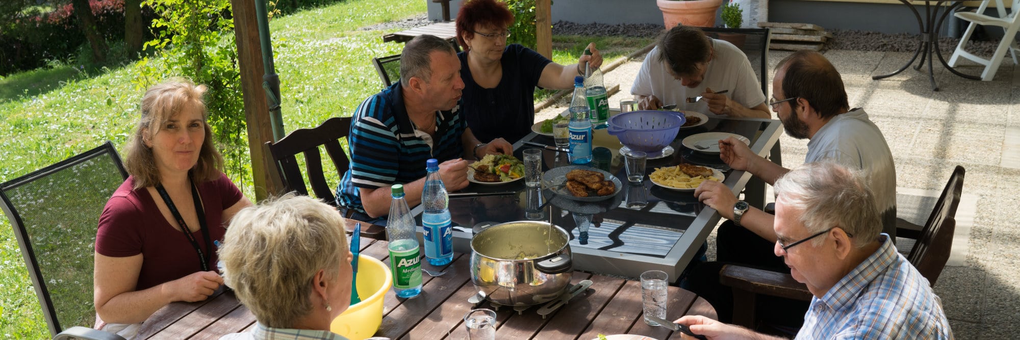Wohnen und Freizeit Eine Gruppe von Menschen sitzt auf der Terrasse an einem Tisch und nimmt gemeinsam eine Mahlzeit ein.