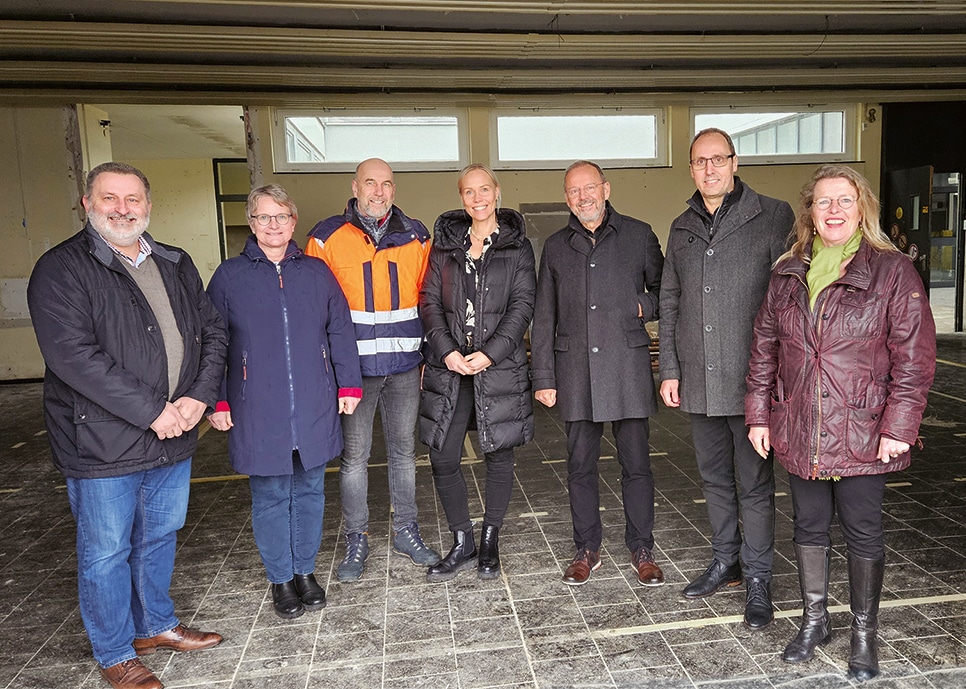 Das Foto zeigt eine Gruppe von Männern und Frauen, die in warmen Jacken in einer offenen Halle stehen, in die Kamera schauen und lächeln.